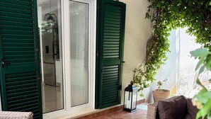 A cozy outdoor seating area with wicker furniture, a glass table with fruit, and a view of a building through green shutters. - Villa Antonija, 50 m from sandy beach, heated pool, max 12 pax (Omis)