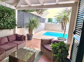 Un porche cubierto con piscina, mobiliario de mimbre y plantas en macetas.
