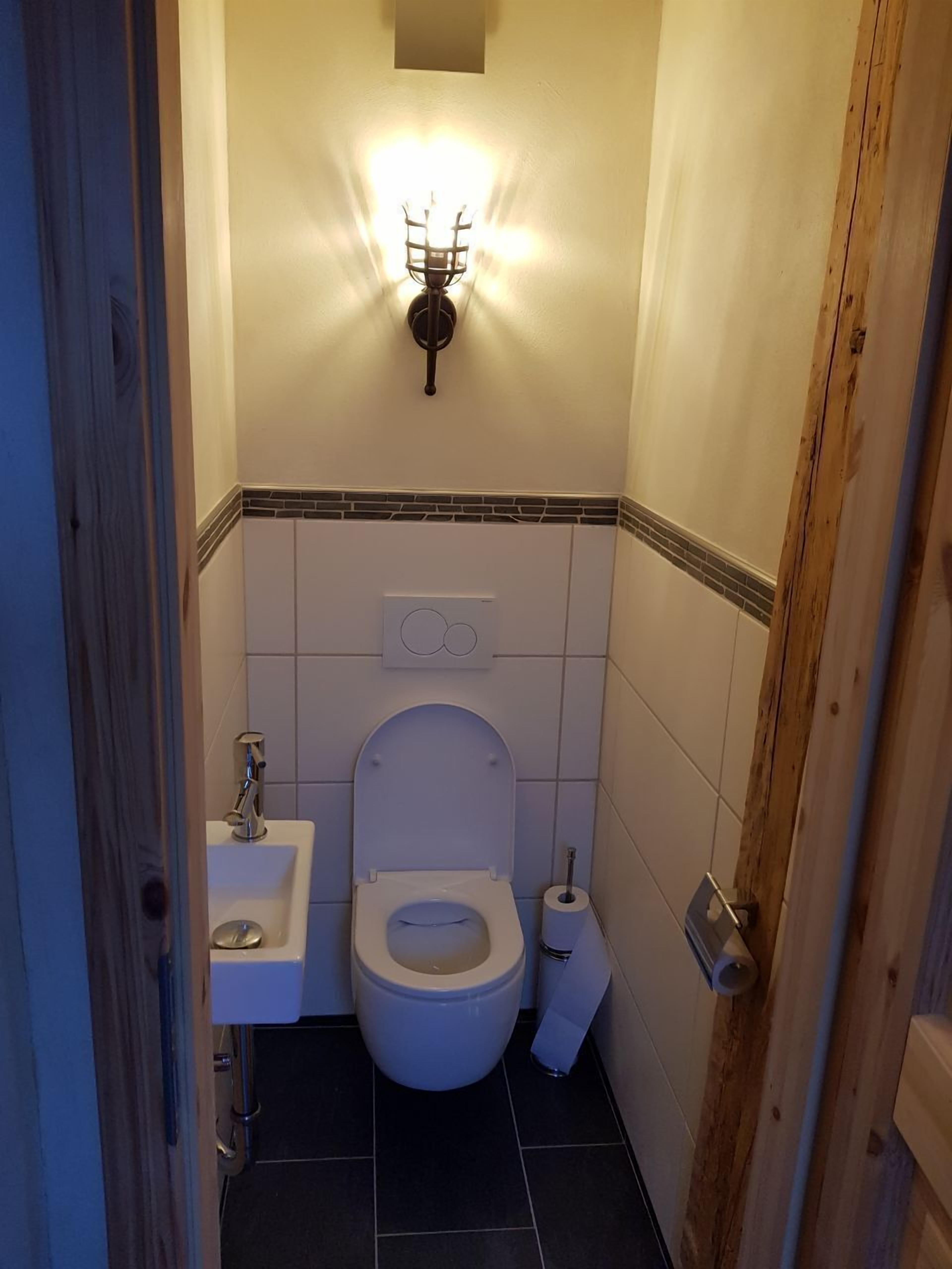 A small, compact bathroom with a toilet, sink, and a wall-mounted light fixture.