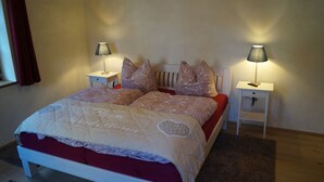 A neatly made bed with a red and white bedspread, two bedside tables with lamps, and a window with curtains.