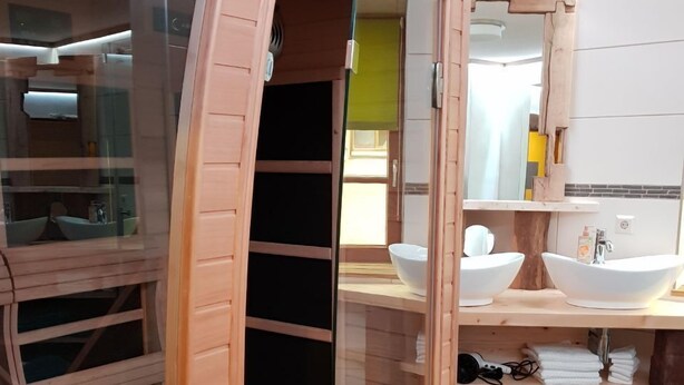 A modern bathroom with a wooden sauna, two sinks, and neatly folded towels on shelves.