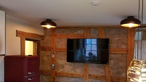 A compact kitchen with a stone wall, a flat-screen TV, and a dining area with a table and chairs.