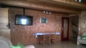 A wooden interior with a TV mounted on the wall, a dining table with chairs, a sofa with a green pillow, and a staircase leading to an upper level. - Former farmhouse in a quiet outskirts. Pets are welcome. (Aichhalden)