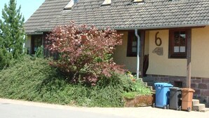 A two-story building with a sloped roof, multiple skylights, and a chimney. There is a small porch area with a door and windows. The building number '6' is visible on the side. - Former farmhouse in a quiet outskirts. Pets are welcome. (Aichhalden)