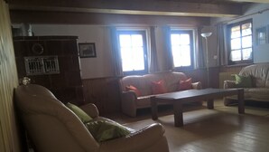 A living room with a sofa, armchair, and a wooden coffee table. There are two windows with curtains, a radiator, and a lamp. - Former farmhouse in a quiet outskirts. Pets are welcome. (Aichhalden)
