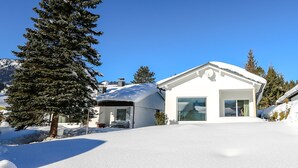 A snow-covered house with a large window and a door, surrounded by snow and trees. - New holiday home in the mountains, Bad Mitterndorf, Sonnenalm (Bad Mitterndorf)