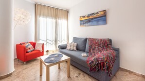 A living room with a sofa, a red armchair, a coffee table, and a painting on the wall. - Central Apartment with Shared Terrace, Wi-Fi, Air Conditioning and TV (MALAGA)