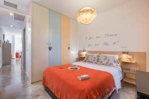 Une chambre moderne avec un grand lit, une citation décorative sur le mur, un luminaire décoratif au plafond et une table de chevet avec une lampe.
