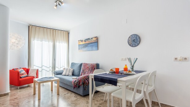 A living room with a sofa, a dining table with chairs, a clock, and a painting on the wall. - Central Apartment with Shared Terrace, Wi-Fi, Air Conditioning and TV (MALAGA)