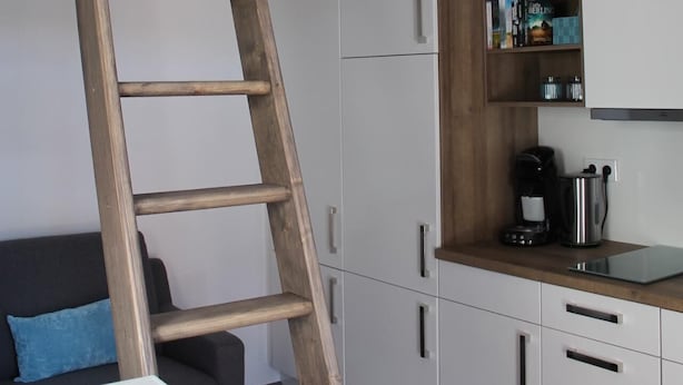 A compact room with a bunk bed, a wooden ladder, a kitchenette, and a small seating area with a cushion. - De Hunk, the small apartment in the town center (Borkum)