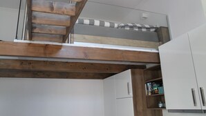 A loft-style bedroom with a wooden staircase, a bunk bed, and white cabinetry. - De Hunk, the small apartment in the town center (Borkum)