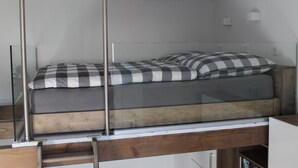 A loft-style bedroom with a glass ceiling, a wooden platform, and a checkered bedspread. - De Hunk, the small apartment in the town center (Borkum)