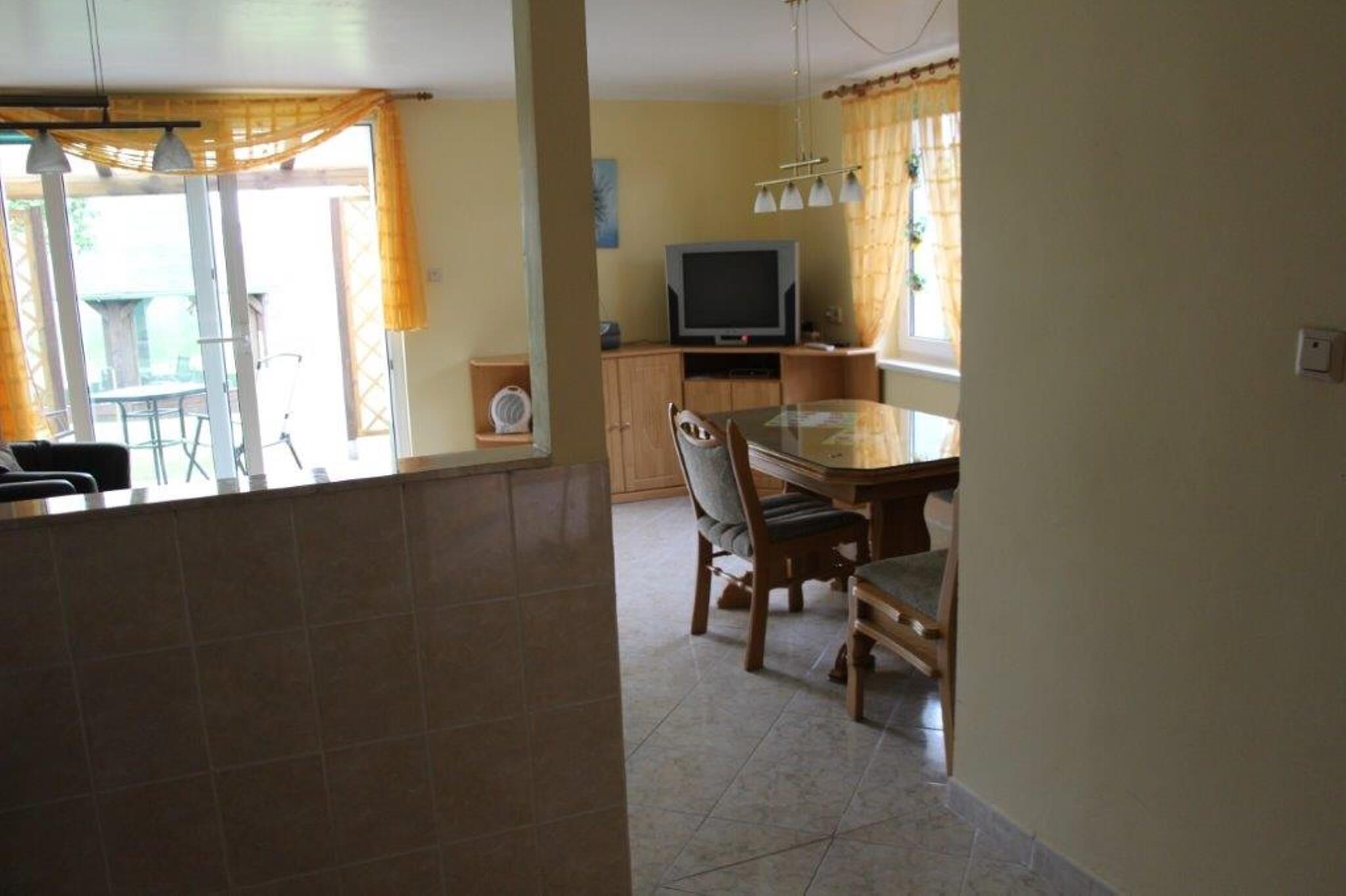 Un coin repas avec une table et des chaises, un téléviseur posé sur un meuble, et une fenêtre avec des rideaux.
