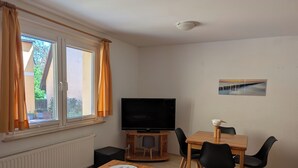 Une pièce avec un téléviseur, des meubles en bois, une table à manger et une fenêtre avec des rideaux.