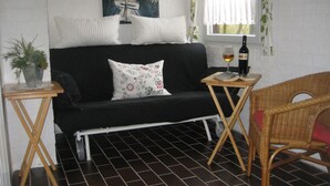 A room with a black sofa, a small table with a bottle and glass, a wicker chair, and a potted plant.