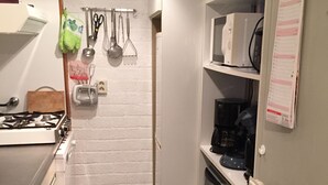 A compact kitchen with a gas stove, white cabinets, a green rug, and various kitchen utensils hanging on the wall.