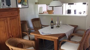 A dining area with a wooden table and wicker chairs, a hanging light fixture, and a view of the outdoors through a window.