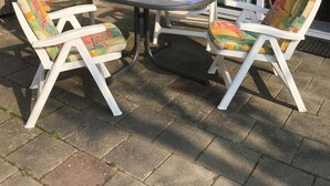 An outdoor patio with a round table, two chairs, and a small table set with cups and a vase of flowers.