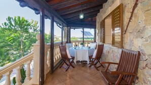 A covered outdoor patio with a stone wall, wooden ceiling, and a table set for two with chairs. - Finca Can Pep (Sant Joan)
