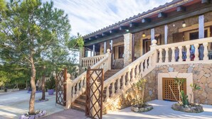 A building with a stone facade, a wooden staircase with balusters, and a gated entrance. - Finca Can Pep (Sant Joan)