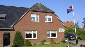 Une maison à deux étages, construite en briques, avec un toit en pente, un mât sur lequel flotte un drapeau, et une enseigne indiquant une réduction de 10 %.