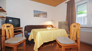 Une pièce confortable avec un canapé, deux chaises en bois, une table avec un saladier, un téléviseur et une fenêtre avec des rideaux.