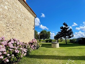 Un edificio de piedra con un jardín delantero, cielo despejado y un árbol grande.