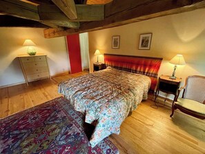 Un dormitorio con una cama, dos mesitas de noche, una silla, un aparador y un tapete estampado.