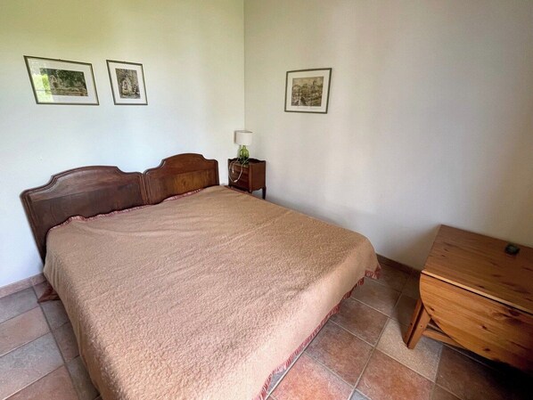A bedroom with a bed, a nightstand, a lamp, and a wooden dresser.
