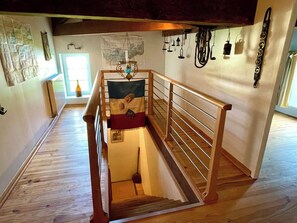 A wooden staircase with a handrail, a small window with a bottle, and a hanging light fixture.