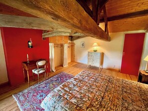 Une chambre avec un grand lit, un bureau avec une chaise, un petit meuble et un mur rouge.