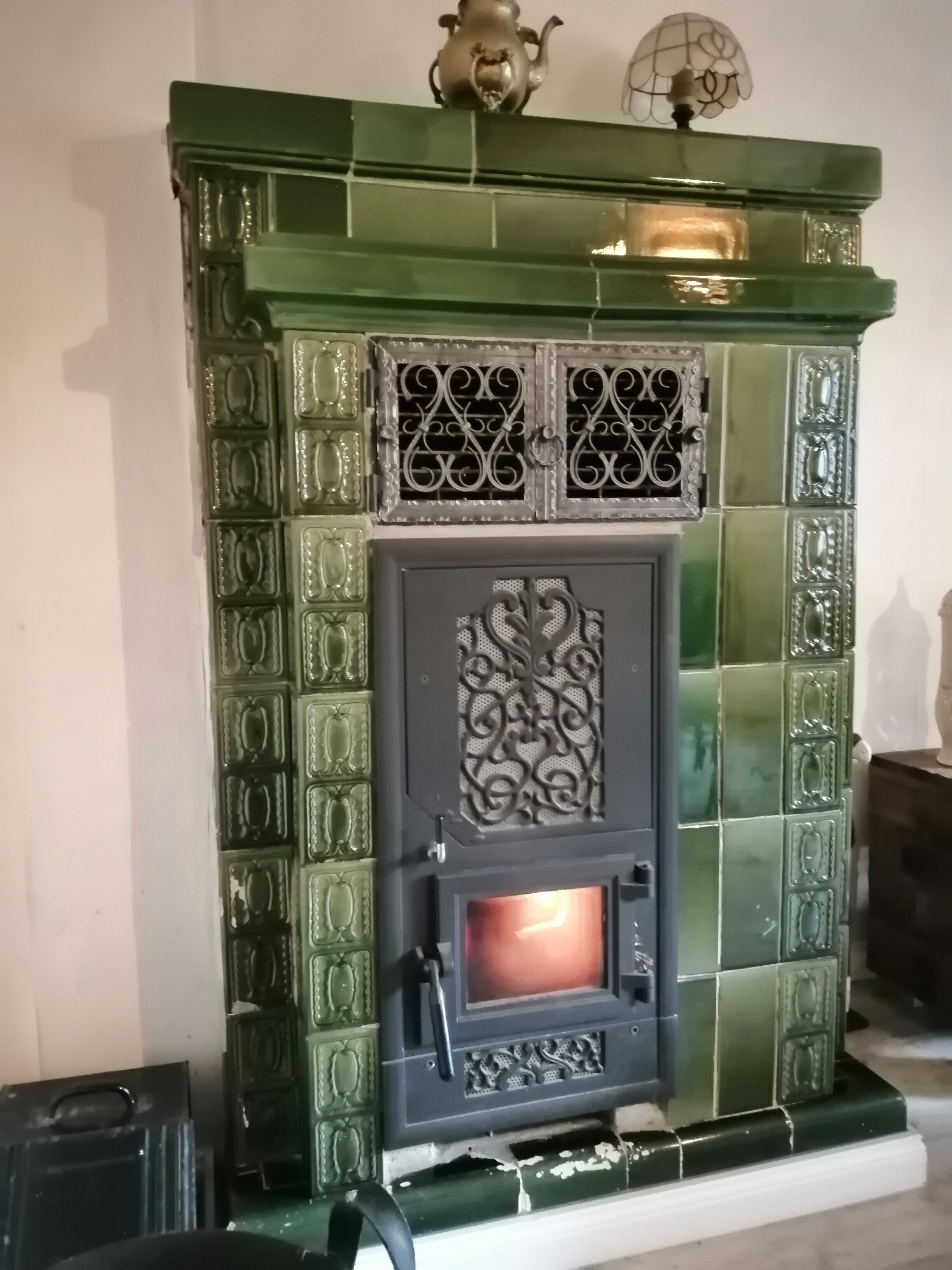 Una chimenea con revestimiento de baldosas verdes, una puerta metálica decorativa y un pequeño estante encima.