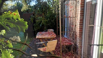 Un jardín con una mesa y sillas, rodeado por un muro de ladrillo y una ventana.