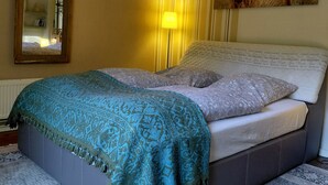 A bedroom with a bed, a bedside lamp, a mirror, a wall-mounted artwork of a bull, and a striped curtain.