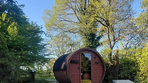 A cylindrical wooden structure with a door, a small bench, and a shed nearby.