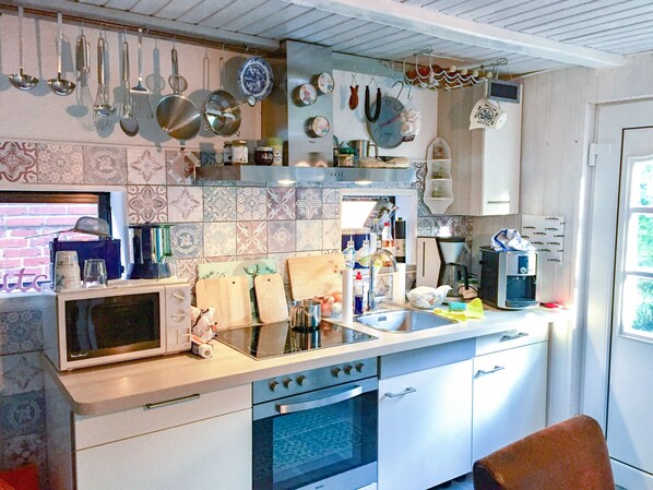Una cocina equipada con microondas, estufa, pileta y diversos utensilios colgando.
