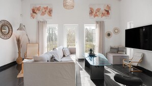 En rummelig opholdsstue med højt til loftet, et sofabord i glas, en sofa og et fjernsyn.