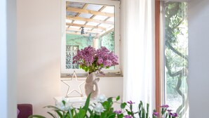 A room with a white console table, a star-shaped decoration, a vase with flowers, and a window with a view of greenery. - "Sea lights" apartment on Sylt for 2 people with garden in the city center (Sylt OT Westerland)