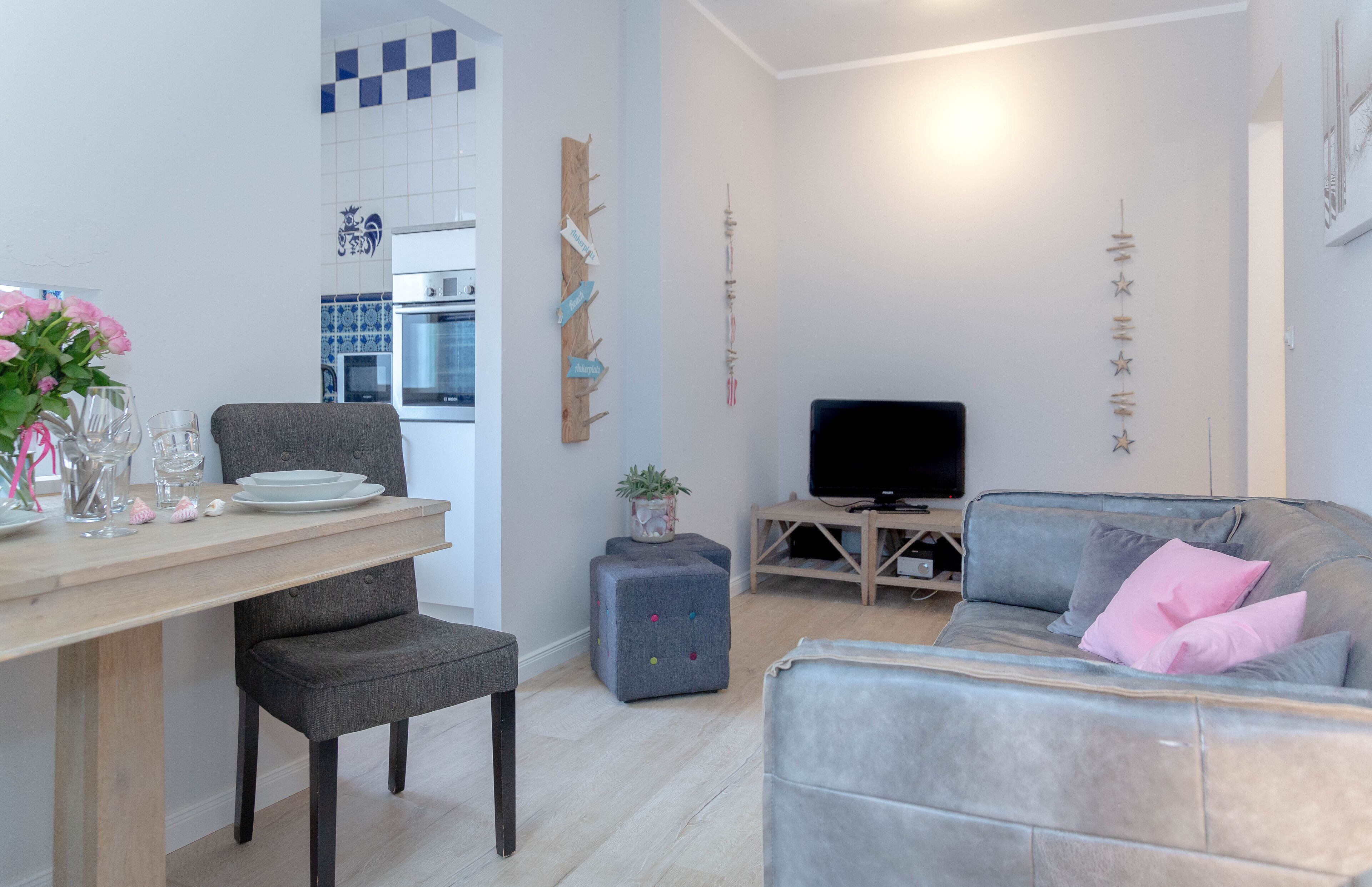 A modern living room with a grey sofa, a small table with a TV, and a dining area with a wooden table and chairs.