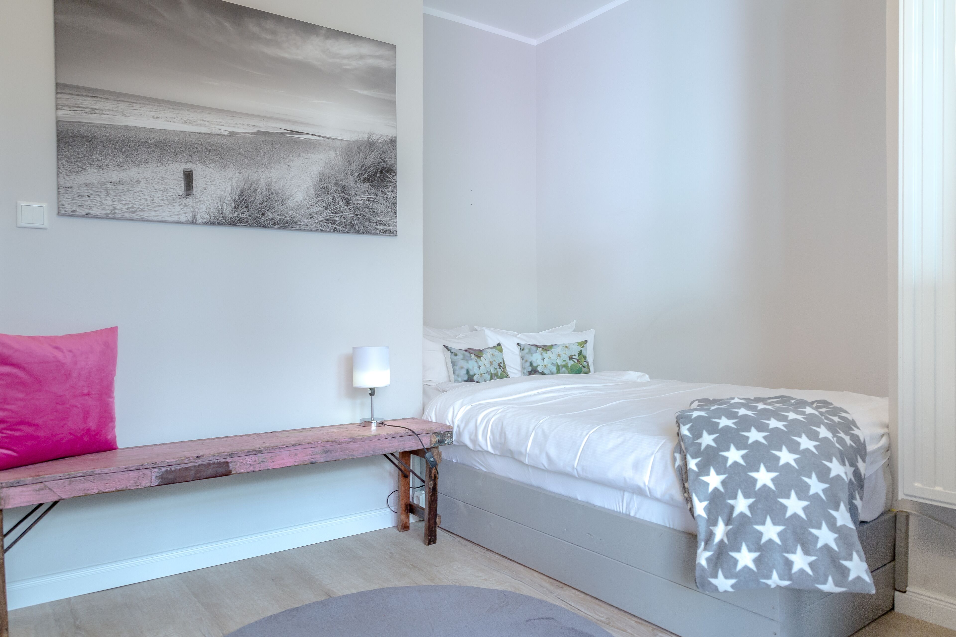 A bedroom with a bed, a bench, a lamp, and a painting on the wall.