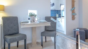 A dining area with a table set for two, two grey upholstered chairs, a wooden table base, a potted plant, and a vase with flowers. - "Sea lights" apartment on Sylt for 2 people with garden in the city center (Sylt OT Westerland)