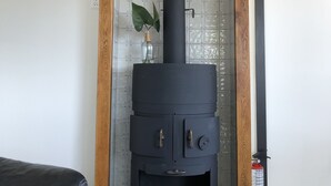 Una estufa de leña negra con dos puertas y una chimenea, ubicada en una esquina debajo de una viga de madera.