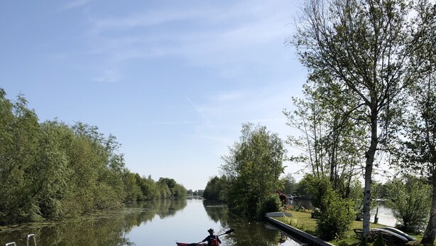 Un patio a orillas del río con una mesa y sillas, un jarrón de flores y vista al río con un kayak.