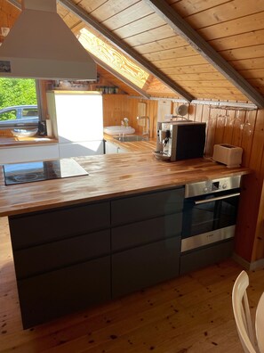 Cocina compacta con armarios de madera, horno Bosch e islote con lavamanos.