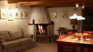 A cozy living room with a fireplace, a wooden dining table, and a sofa. -  Renovated in 2006, charming holiday home by the woods (Samone)