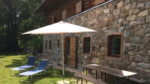 A stone building with a wooden exterior, a covered patio with a table and chairs, and a grill area. -  Renovated in 2006, charming holiday home by the woods (Samone)