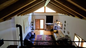 An attic room with a high ceiling, wooden beams, a sofa, a small table, a lamp, and a view of the adjacent room through a doorway. -  Renovated in 2006, charming holiday home by the woods (Samone)