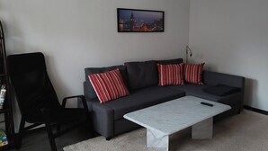 A living room with a dark grey sofa, red and white striped pillows, a white coffee table, and a framed cityscape picture on the wall.