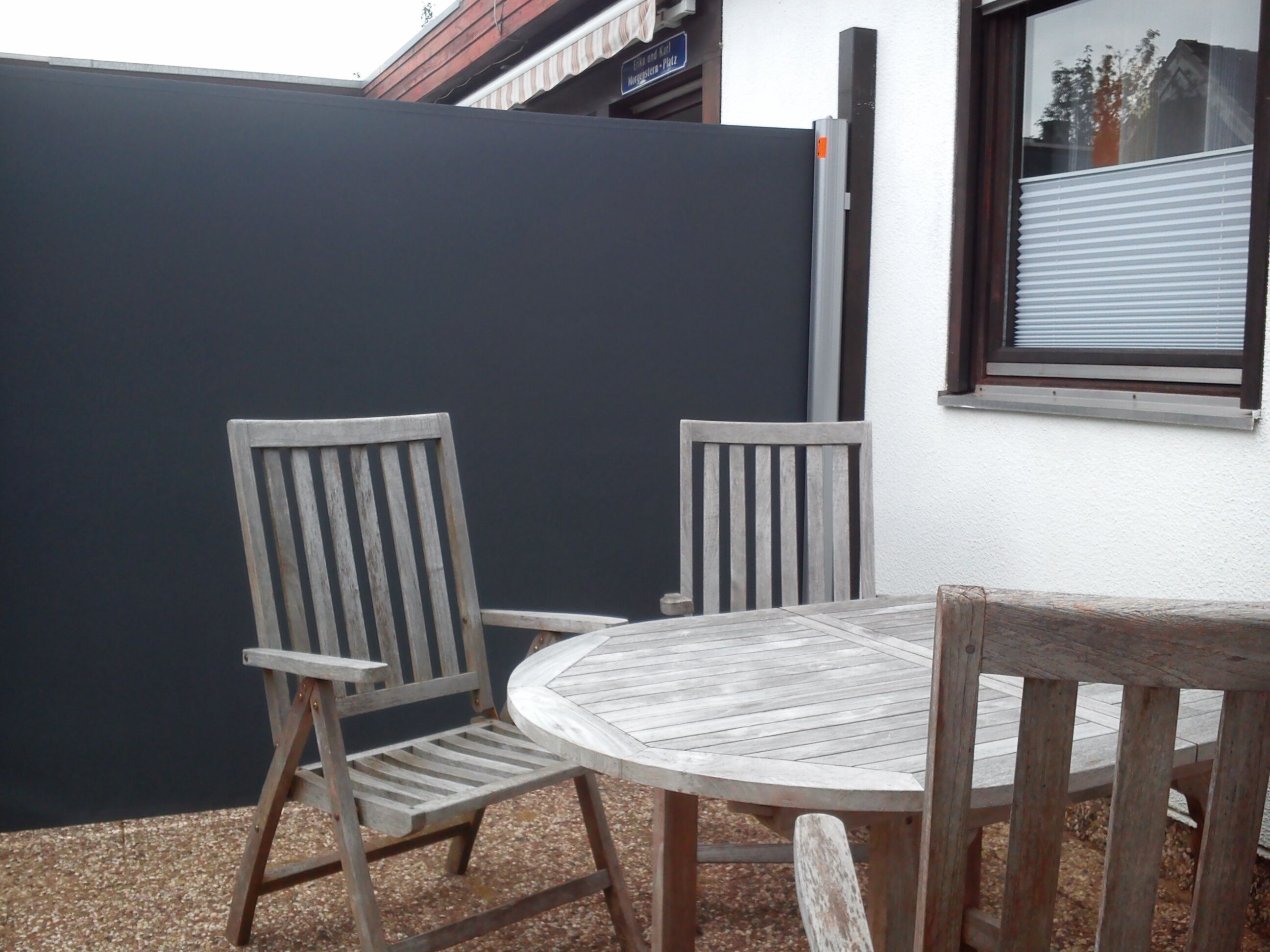 A round wooden table with two chairs, a dark wall, and a window with blinds.