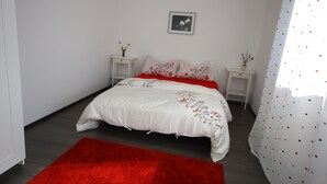 A bedroom with a bed, a red rug, white walls, and a picture on the wall.